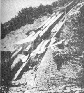 Black-and-white photograph of the ruptured Oigawa penstock on a steep hillside, with broken pipe sections scattered down the slope